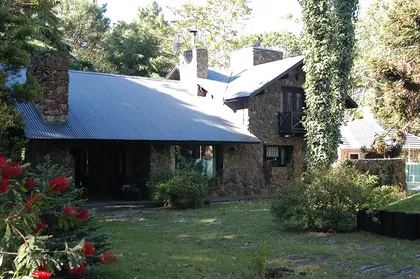 Fachada rústica de casa de piedra rodeada de bosque — proyecto Casa Cariló 1997, por Hugo Zawadski Arquitectos, en Cariló