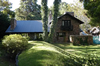 Fachada rústica con piedra y vegetación exuberante — proyecto Casa Cariló 1997, por Hugo Zawadski Arquitectos, en Cariló