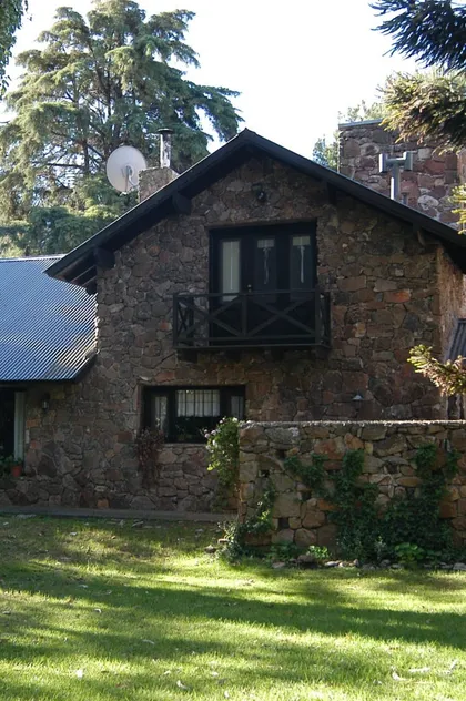 Fachada rústica de piedra con balcón de madera — proyecto Casa Cariló 1997, por Hugo Zawadski Arquitectos, en Cariló