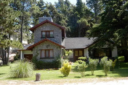 Fachada rústica de casa con ladrillos, vigas de madera y jardín — proyecto Casa Cariló 2003 - 2, por Hugo Zawadski Arquitectos, en Cariló
