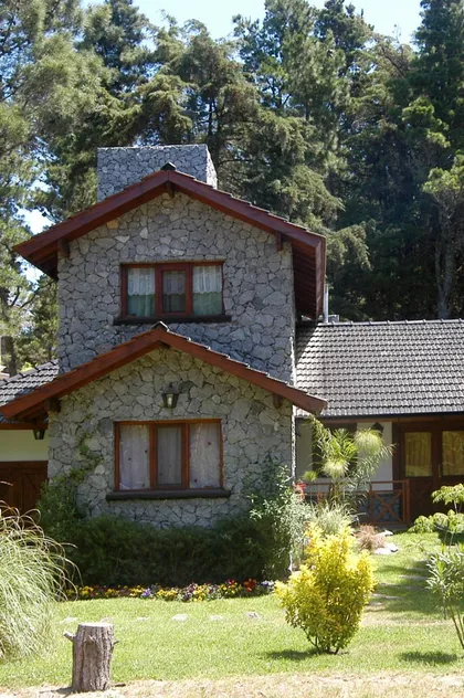 Fachada de casa rústica de piedra con bosque — proyecto Casa Cariló 2003 - 2, por Hugo Zawadski Arquitectos, en Cariló