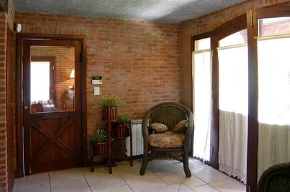 Sala de estar rústica con paredes de ladrillo expuesto y sillón de mimbre — proyecto Casa Cariló 2004, por Hugo Zawadski Arquitectos, en Cariló