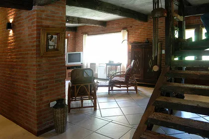 Sala rústica con ladrillos expuestos y vigas de madera — proyecto Casa Cariló 2004, por Hugo Zawadski Arquitectos, en Cariló