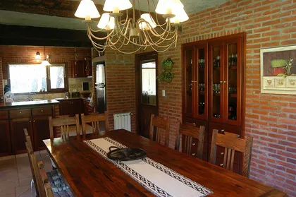 Comedor rústico con ladrillos expuestos y cocina adyacente — proyecto Casa Cariló 2004, por Hugo Zawadski Arquitectos, en Cariló