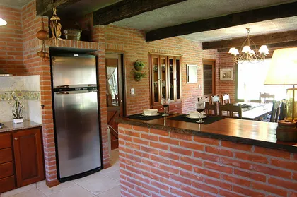 Cocina rústica con paredes de ladrillo visto y vigas de madera — proyecto Casa Cariló 2004, por Hugo Zawadski Arquitectos, en Cariló