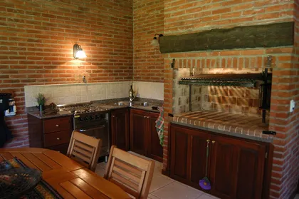 Cocina rústica con parrilla de ladrillos y mueble de madera — proyecto Casa Cariló 2004, por Hugo Zawadski Arquitectos, en Cariló