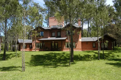 Fachada de casa de campo de ladrillo rojo con árboles y césped — proyecto Casa Cariló 2004, por Hugo Zawadski Arquitectos, en Cariló