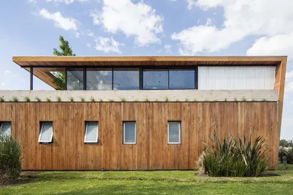 Fachada moderna de madera con grandes ventanales y vegetación — proyecto Santa Isabel, por Arfuso Arquitectos, en Ingeniero Maschwitz