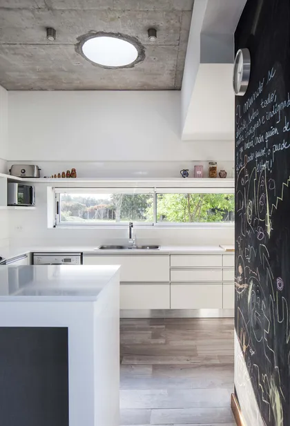 Cocina moderna con isla blanca, techo de hormigón y pared de pizarra — proyecto Santa Isabel, por Arfuso Arquitectos, en Ingeniero Maschwitz