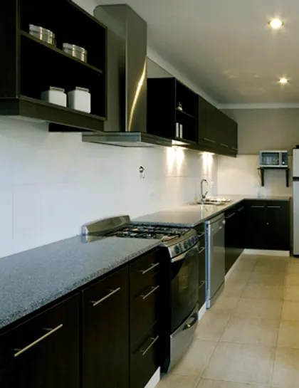 Cocina moderna con gabinetes de madera oscura y mesada de piedra gris — proyecto Casa Cariló 2007, por Hugo Zawadski Arquitectos, en Cariló