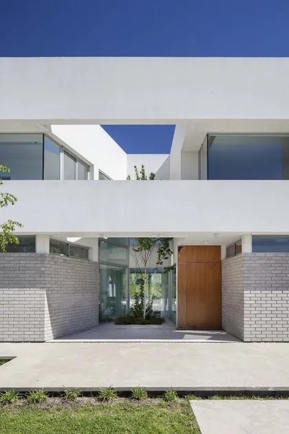 Fachada moderna blanca con entrada de madera y jardín interior — proyecto Casa MA, por Estudio GR, en City Bell