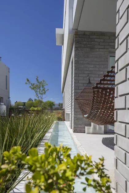 Pati exterior moderno con hamaca colgante de rattan y fuente lineal — proyecto Casa MA, por Estudio GR, en City Bell