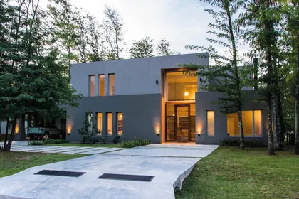 Casa minimalista gris con ventanales iluminados entre árboles al atardecer — proyecto Casa 18, por Parrado Arquitectura