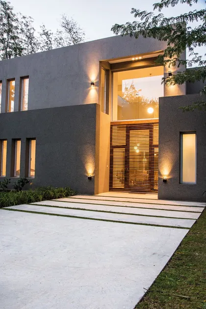 Fachada contemporánea gris con entrada iluminada y grandes ventanales — proyecto Casa 18, por Parrado Arquitectura