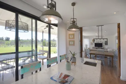 Comedor moderno con isla, ventanales hacia el campo y lámparas colgantes — proyecto Casa 16, por Parrado Arquitectura