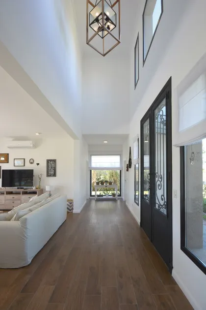 Pasillo moderno con doble altura, piso de madera y puerta negra — proyecto Casa 16, por Parrado Arquitectura
