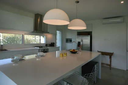Cocina moderna con isla central, mesada blanca y lámparas colgantes — proyecto Casa 17, por Parrado Arquitectura