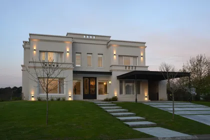 Casa moderna blanca con fachada iluminada al atardecer y jardín verde — proyecto Casa 17, por Parrado Arquitectura