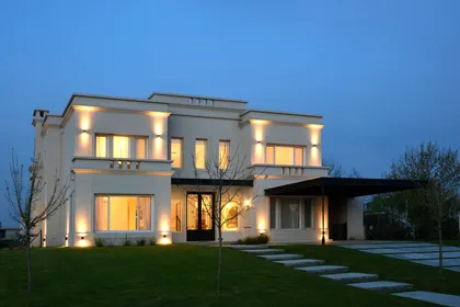 Casa contemporánea blanca iluminada al atardecer con jardín y galería — proyecto Casa 17, por Parrado Arquitectura