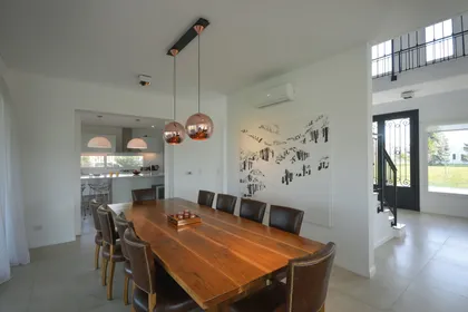 Comedor moderno con mesa de madera, lámparas cobre y doble altura — proyecto Casa 17, por Parrado Arquitectura