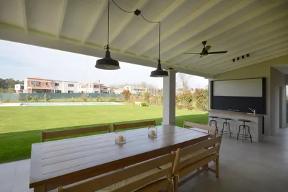 Quincho moderno con mesa de madera, vistas al jardín y campos abiertos — proyecto Casa 17, por Parrado Arquitectura