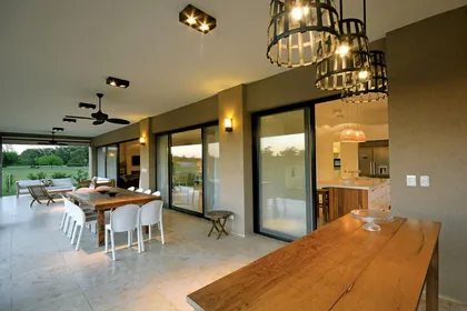 Comedor amplio con mesada madera, ventanales grandes y cocina abierta — proyecto Casa 15, por Parrado Arquitectura