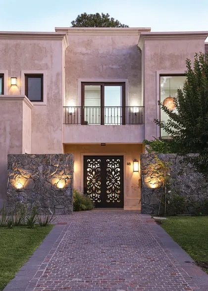 Fachada contemporánea rosa con puerta ornamental negra iluminada — proyecto SD 48, por Estudio Arq Daniel Tarrio