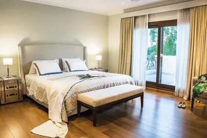 Dormitorio luminoso con cama tapizada, piso de madera y balcón — proyecto TRV 164, por Estudio Arq Daniel Tarrio