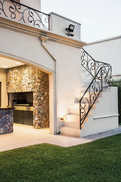 Casa contemporánea con escalera de hierro negro y fachada de piedra iluminada — proyecto TRV 164, por Estudio Arq Daniel Tarrio