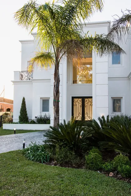 Casa blanca contemporánea con palmera y frondoso jardín delantero — proyecto TRL 9, por Estudio Arq Daniel Tarrio
