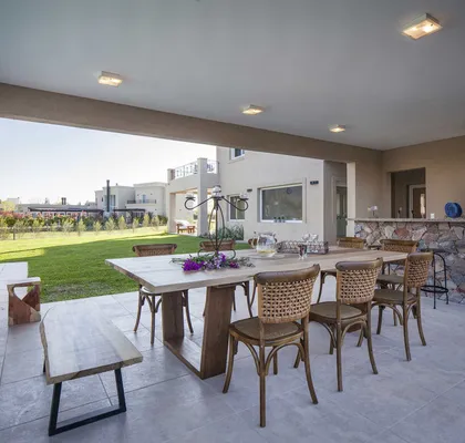 Amplio patio con comedor de madera, sillas de mimbre y jardín verde al fondo — proyecto TRV 137, por Estudio Arq Daniel Tarrio