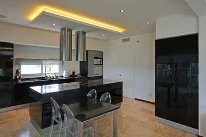 Cocina moderna con isla central negra y mesadas de mármol, luces cálidas — proyecto TRV 487, por Estudio Arq Daniel Tarrio