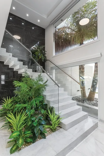 Escalera blanca con plantas verdes y doble altura con ventanal — proyecto TRV 490, por Estudio Arq Daniel Tarrio