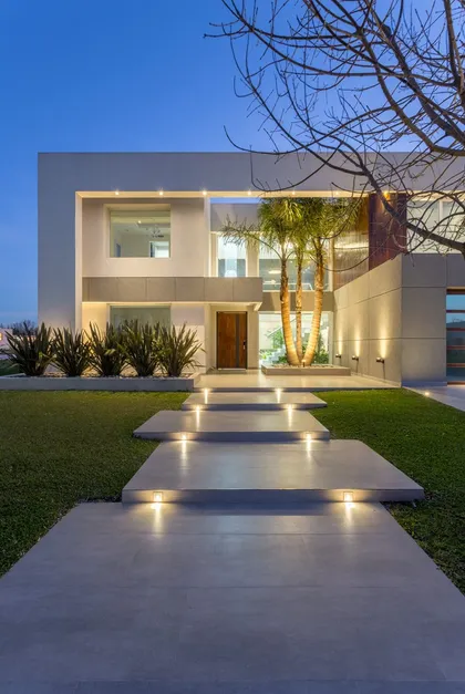 Fachada minimalista de casa moderna con sendero iluminado y jardin — proyecto TRV 490, por Estudio Arq Daniel Tarrio