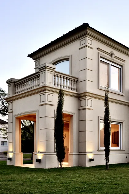 Casa moderna de fachada blanca con balcón y cipreses iluminada — proyecto Ayres del Pilar, por Marconi Silva Arquitectos, en Pilar