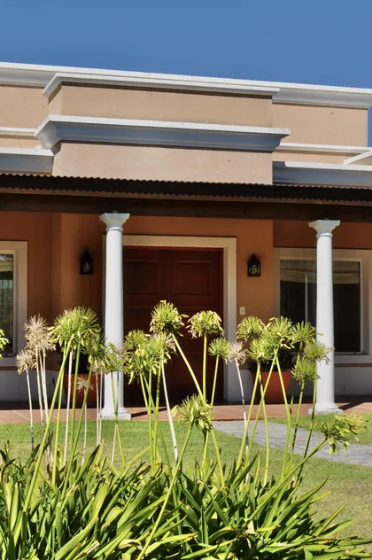 Fachada terracota con columnas blancas y plantas altas al frente — proyecto Chacras de la Cruz, por Marconi Silva Arquitectos, en Capilla del Señor