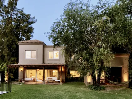 Casa moderna con jardin, pergola iluminada al atardecer y arboles — proyecto El Encuentro , por Marconi Silva Arquitectos, en Benavidez