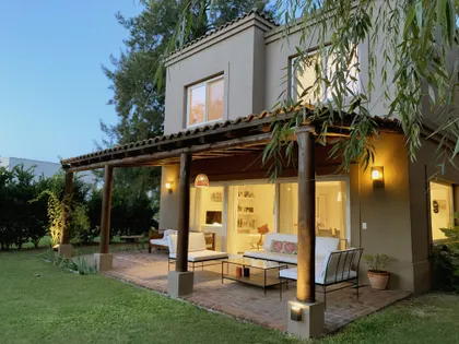 Casa contemporánea con galería cubierta, iluminada al atardecer en jardín verde — proyecto El Encuentro , por Marconi Silva Arquitectos, en Benavidez