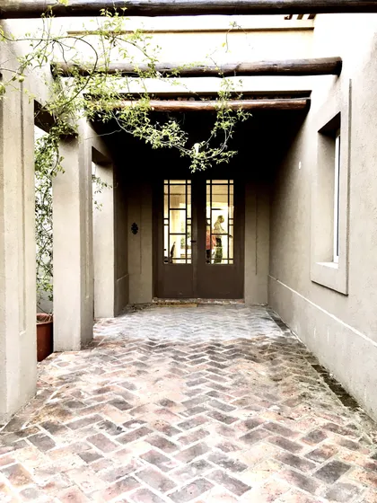 Pasillo cubierto con pergola de vigas madera hacia puerta principal — proyecto El Encuentro , por Marconi Silva Arquitectos, en Benavidez