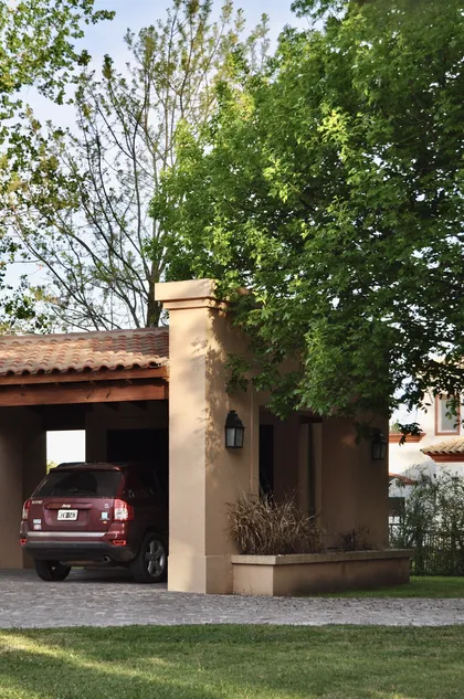 Casa contemporánea con cochera integrada y vegetación frondosa — proyecto El Solar de Capilla, por Marconi Silva Arquitectos, en Capilla del Señor