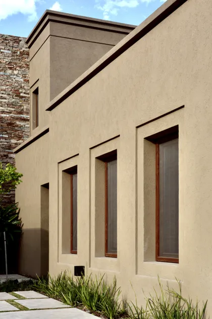 Fachada minimalista beige con ventanales altos y ladrillo visto lateral — proyecto Golf Club Nordelta, por Marconi Silva Arquitectos, en Nordelta