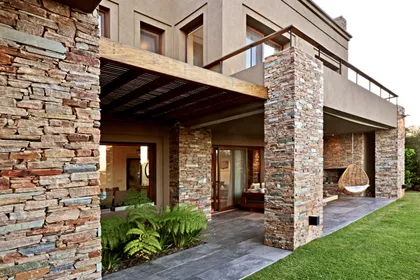 Fachada contemporánea con galerías, piedra natural y ventanales amplios — proyecto Golf Club Nordelta, por Marconi Silva Arquitectos, en Nordelta