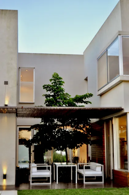 Patio contemporaneo con pergola negra, muebles blancos y arbol central — proyecto Haras Santa María, por Marconi Silva Arquitectos, en Escobar