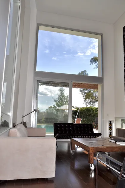 Living con ventanal sobre piscina y jardín, techo doble altura — proyecto Haras Santa María, por Marconi Silva Arquitectos, en Escobar