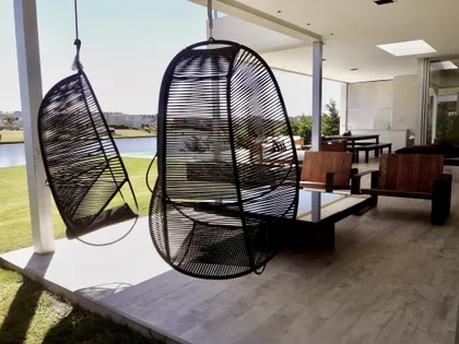 Terraza moderna con sillones colgantes negros y vista al jardín — proyecto Lagos del Golf, por Marconi Silva Arquitectos, en Nordelta