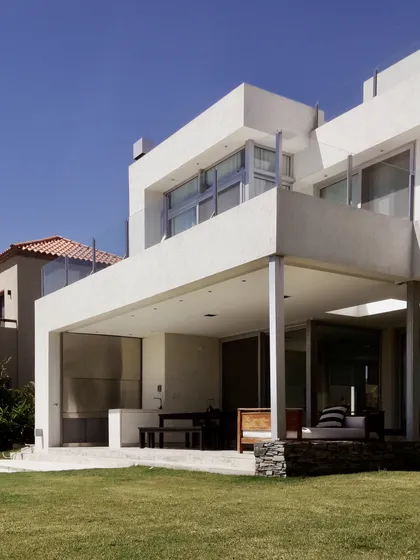 Casa moderna blanca con galería cubierta y jardín frontal impecable — proyecto Lagos del Golf, por Marconi Silva Arquitectos, en Nordelta