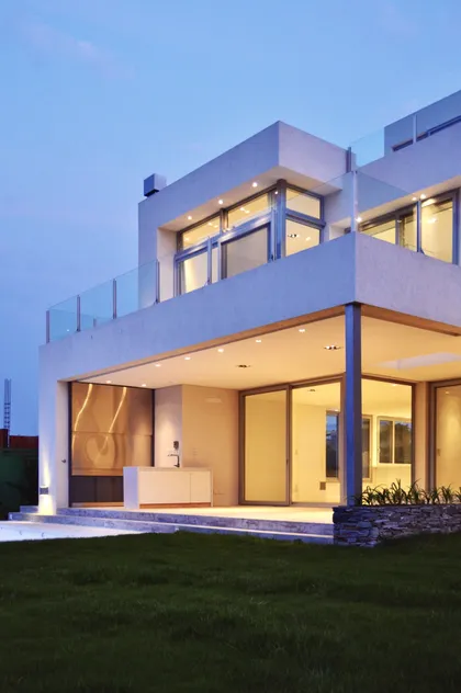 Casa contemporánea de dos plantas con fachada blanca iluminada al atardecer — proyecto Lagos del Golf, por Marconi Silva Arquitectos, en Nordelta