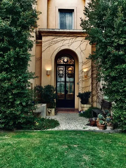 Entrada classica con puerta negra y enredadera verde en fachada — proyecto Lagos del Norte, por Marconi Silva Arquitectos, en Don Torcuato