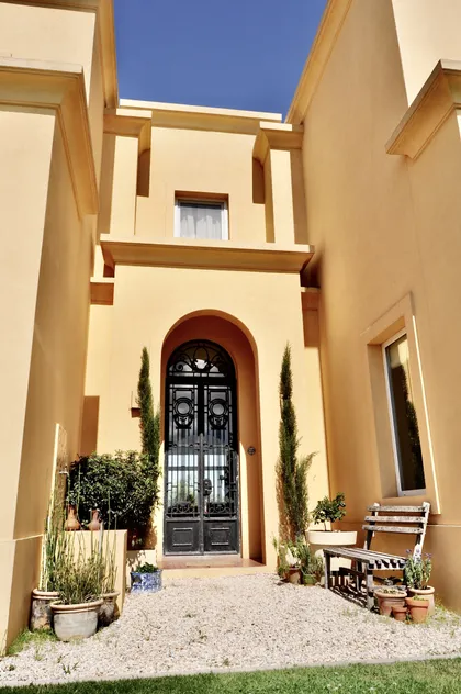 Fachada con arco, plantas ciprés y puerta negra en patio — proyecto Lagos del Norte, por Marconi Silva Arquitectos, en Don Torcuato