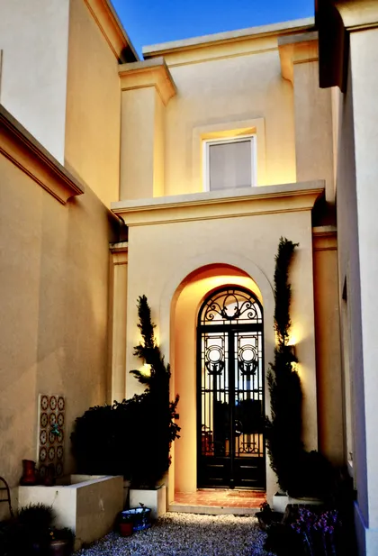 Entrada iluminada con puerta de hierro negro y plantas oscuras silueteadas — proyecto Lagos del Norte, por Marconi Silva Arquitectos, en Don Torcuato